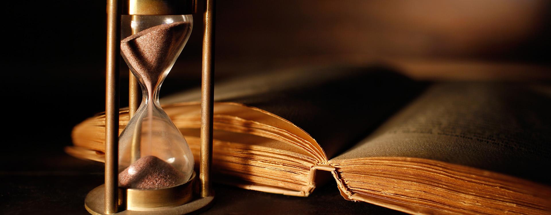 Old book on wooden desk with sand timer